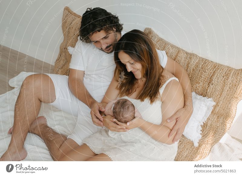 Loving couple admiring newborn baby admire home bedroom embrace tender parent love family man woman together hug mother father child infant rest comfort