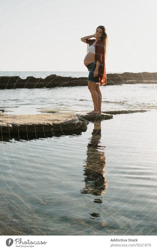 Pregnant female standing on stone near sea woman pregnant shore morning rest water summer rock rough nature coast relax ocean sunrise dawn casual pregnancy