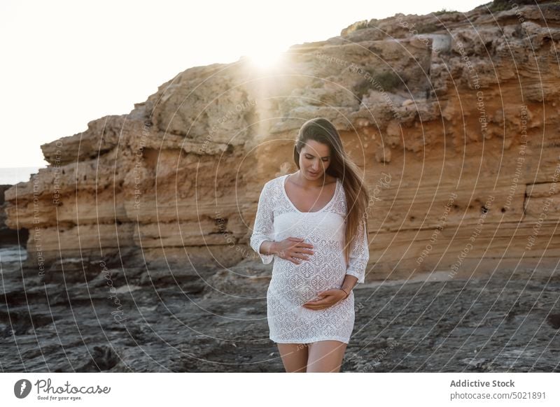 Pregnant woman standing near sandstone cliff summer nature pregnant touch belly expect maternal female anticipate prenatal gentle pregnancy motherhood dress