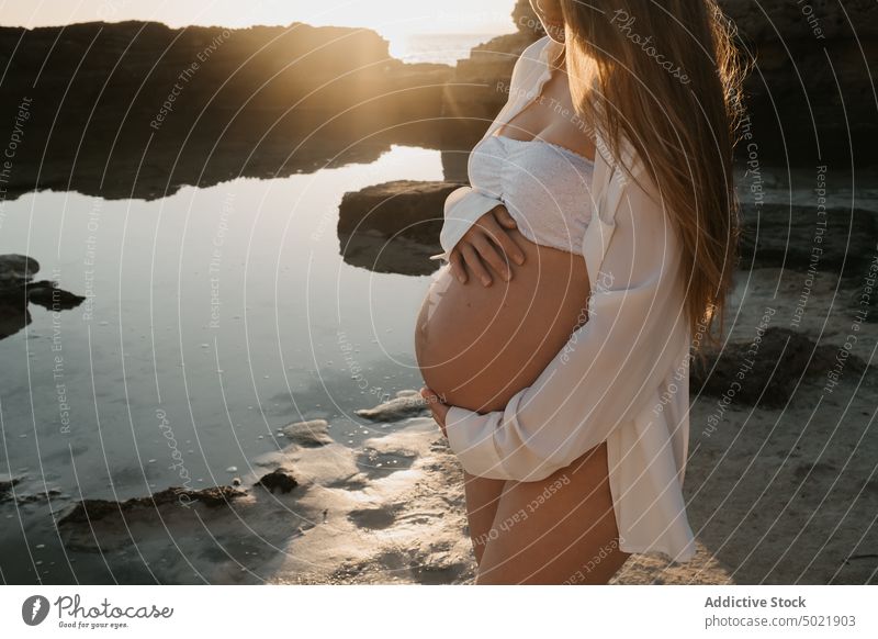 Anonymous pregnant woman touching belly near sea water sunrise rest nature summer shore female love calm relax tummy sky cloudless morning peaceful idyllic