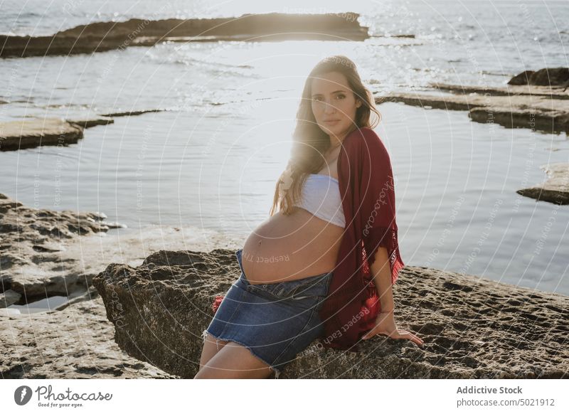 Pregnant female leaning on stone near sea woman pregnant shore morning rest water summer rock rough nature coast relax ocean sunrise dawn casual pregnancy