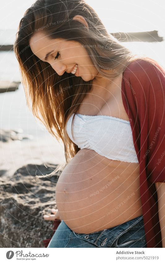 Smiling pregnant female leaning on stone near sea woman shore morning rest water summer rock rough nature coast relax ocean sunrise dawn casual pregnancy mother