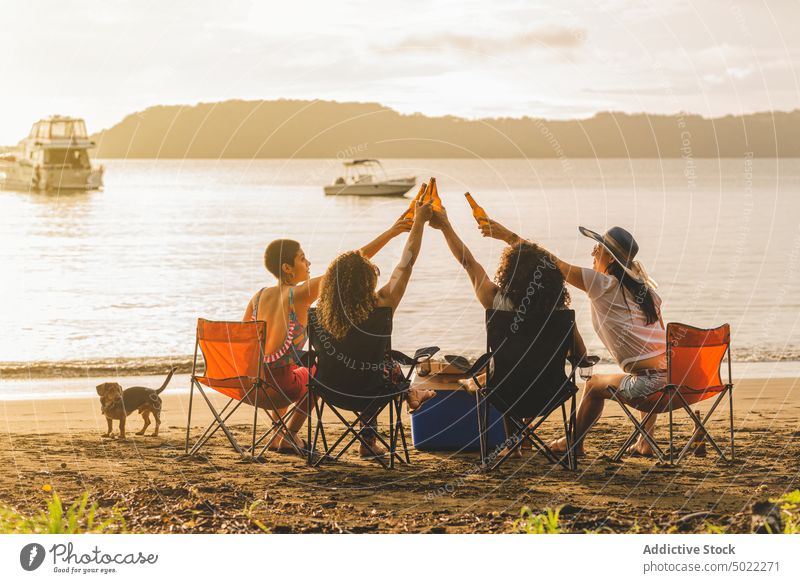 Young people with beer enjoying summer picnic on beach friend clink bottle cheerful gather hangout together happy group young drink friendship toast party