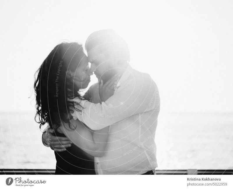 Portrait of young attractive couple dancing latin bachata near sea or ocean. Sunlight background. Man gently hugs his beloved girl and looks at her with admiration