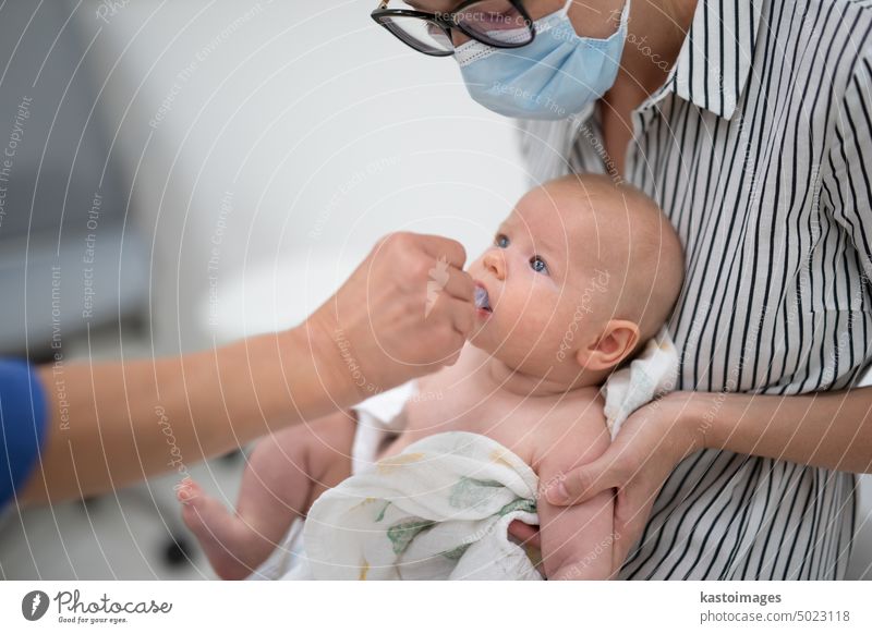 Pediatrician administring oral vaccination against rotavirus infection to little baby in presence of his mother. Children health care and disease prevention
