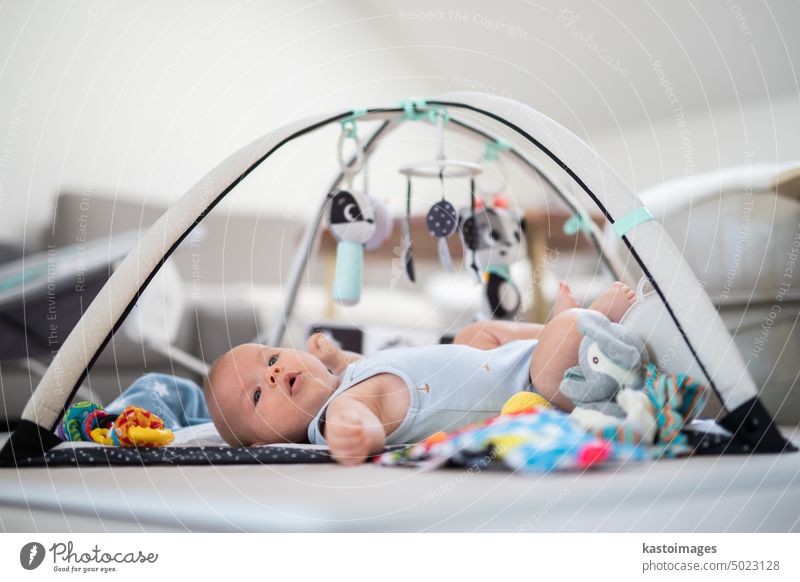 Cute baby boy playing with hanging toys arch on mat at home Baby activity and play center for early infant development. Baby playing at home newborn childhood