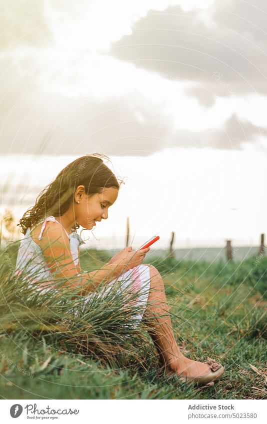 Hispanic girl browsing on smartphone in field sunset happy rest weekend grass summer cheerful joy positive countryside gadget device nature lifestyle smile