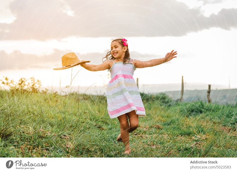 Cheerful girl in grassy field morning countryside happy smile rest weekend summer kid meadow child nature joy cheerful glad dress hat touch head carefree