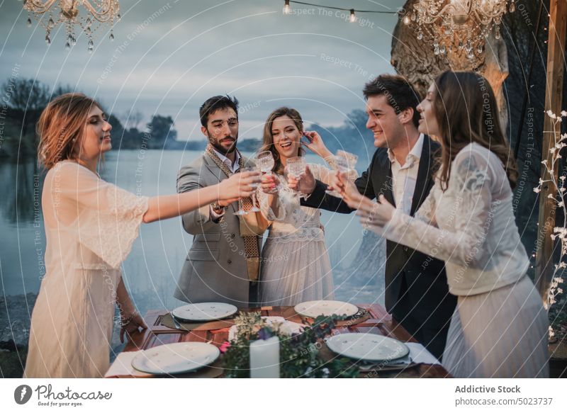Couple doing a toast with happy friends, decorations, table and bride groom couple hugging celebrating glasses lake wedding man woman dress guy lady