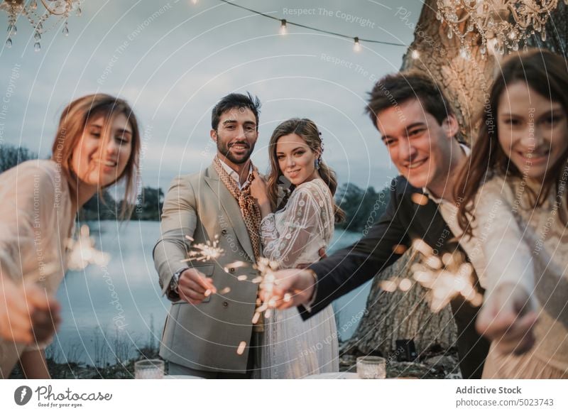 Couple hugging near happy friends, decorations, table and lake couple wedding man woman dress guy lady firework sparkles embracing tree young love marriage