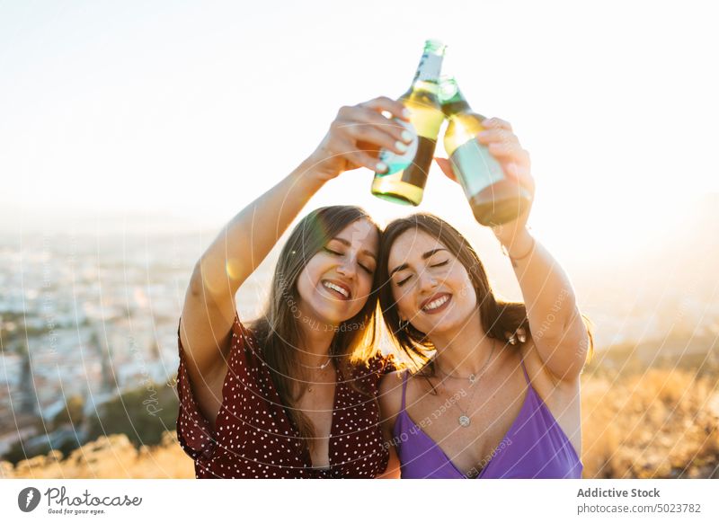 Smiling friends clinking bottles of beer on mount peak women girlfriend nature party alcohol drink toast female cheers eyes closed glass mountain together