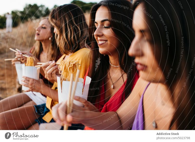 Joyful women having Asian food for lunch in nature girlfriend eat fun box noodle asian food meal chopstick stone border takeaway to go female cheerful cloudless