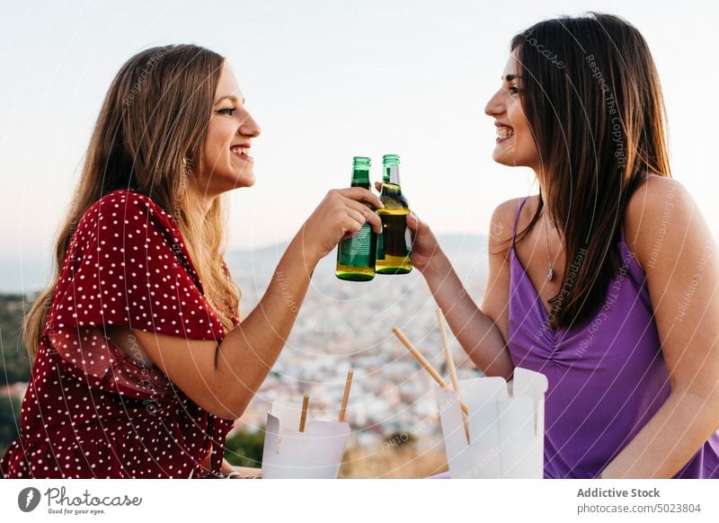 Happy friends clinking bottles drinking beer women gather nature coast alcohol cheerful female happy beverage stone border glass together cheers celebrate booze