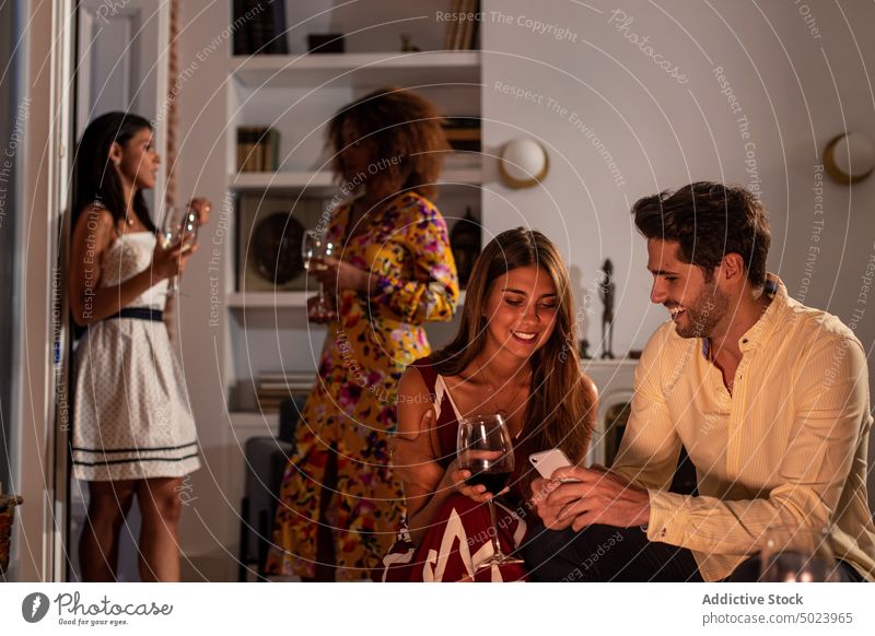 Happy couple using smartphone at party with friend on the background share photo cellphone rest together home communication connection online internet device