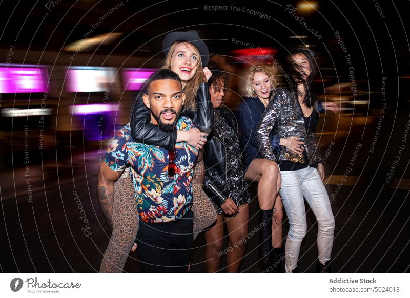 Diverse smiling friends walking on street at night women man piggyback party cheerful style fun cool holiday gather happy celebrate event nightlife positive