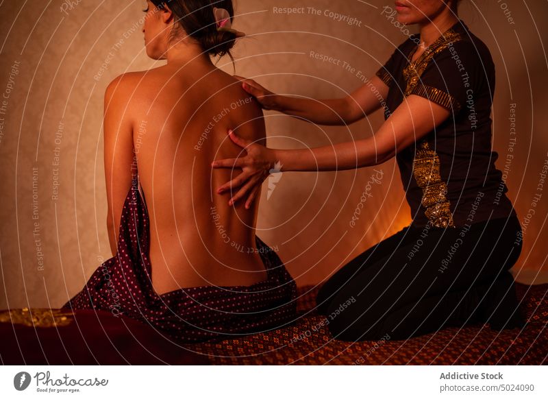 Thai female massagist giving a massage to a young woman masseur massaging thai massage treatment therapy asian spa body orchid flower wellness care beauty