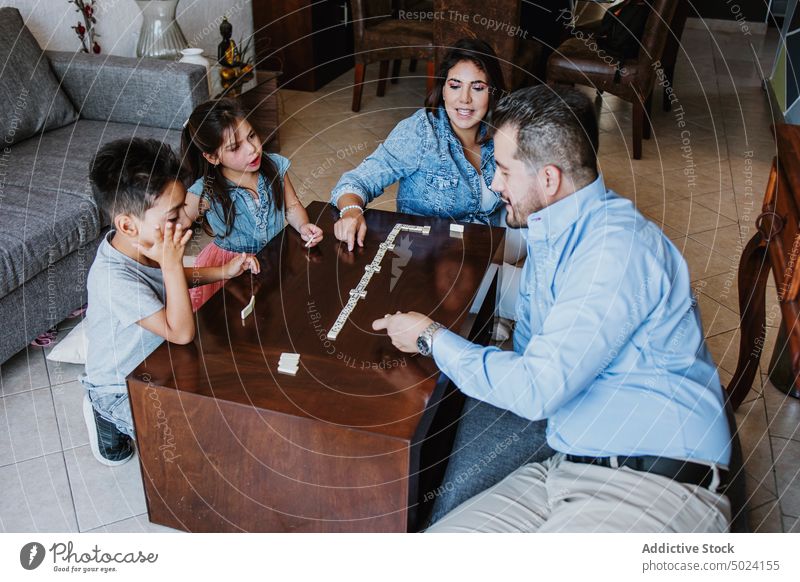 Delighted ethnic family smiling while playing board game during weekend at home woman children tile concentrate together mother free time strategy entertain