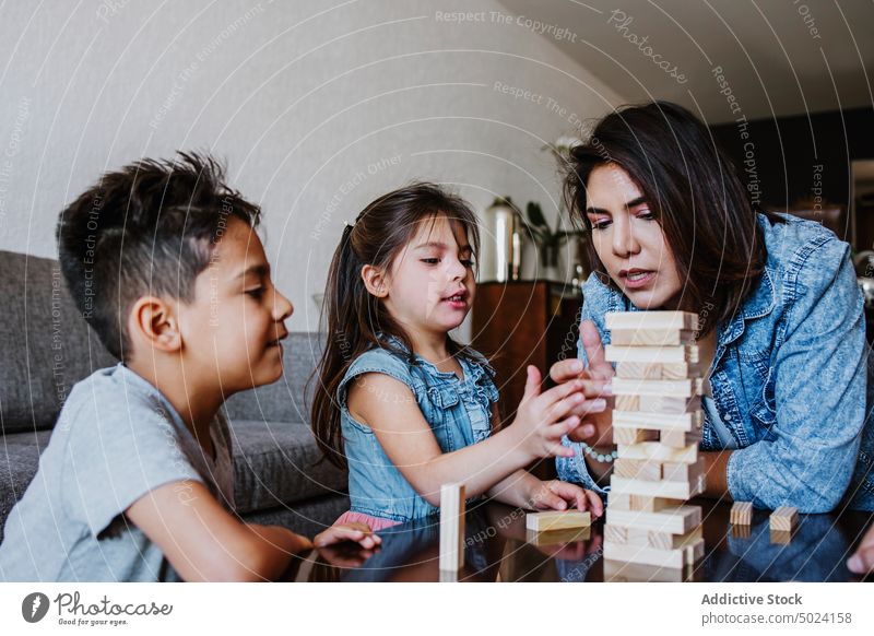 Young ethnic mother with children playing tower game at home woman concentrate together free time strategy entertain board game enjoy love young kid