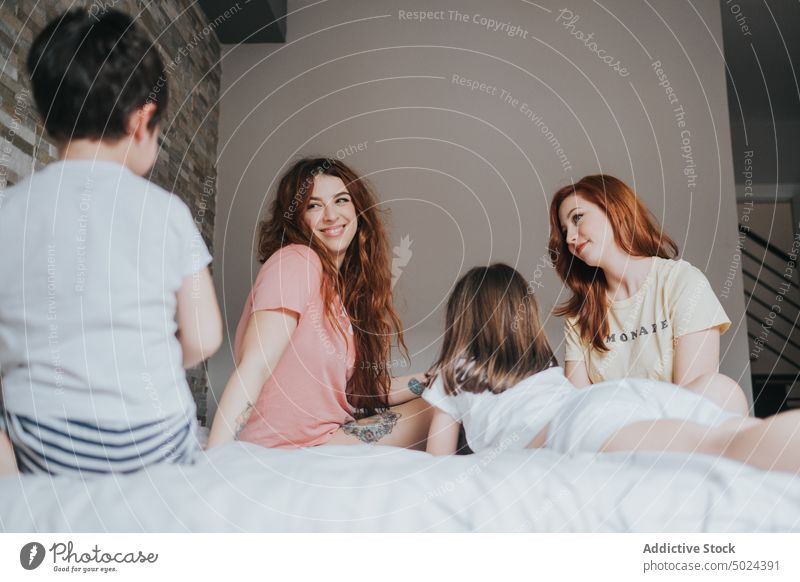 Smiling Women Sitting On Bed With Children indoors woman bed bedroom alternative cheerful childhood children comfort cozy domestic female friendship from below