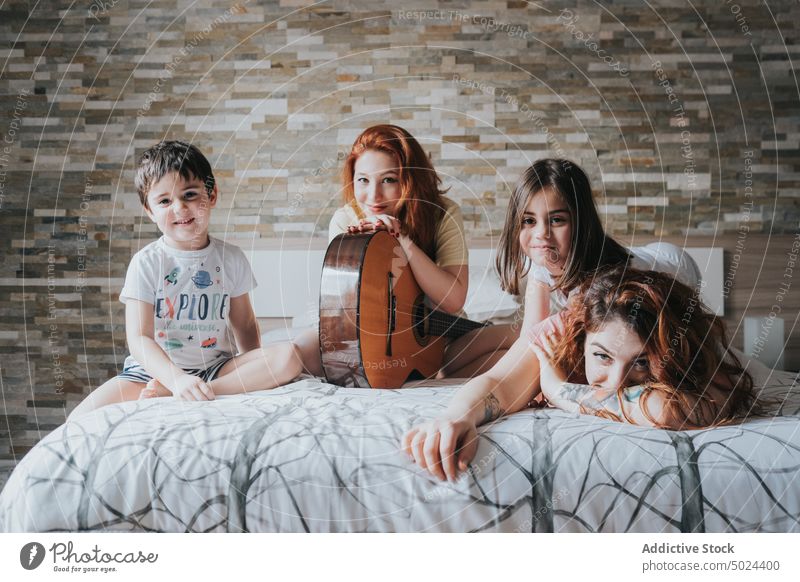 Smiling Women With Guitar Sitting On Bed With Children woman fun friendship indoors alternative bed bedroom cheerful childhood children comfort cozy domestic