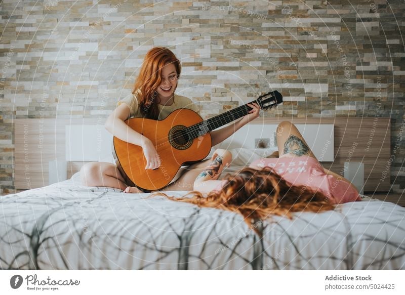 Smiling Women Resting On Bed And Playing On Guitar music bed guitar woman bedroom indoors leisure acoustic alternative art cheerful comfort couple cozy female