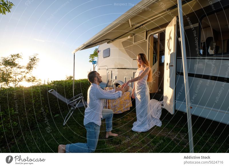 Man making proposal for woman standing near camper in nature couple propose bride groom travel love holding hands together sunset romantic relationship