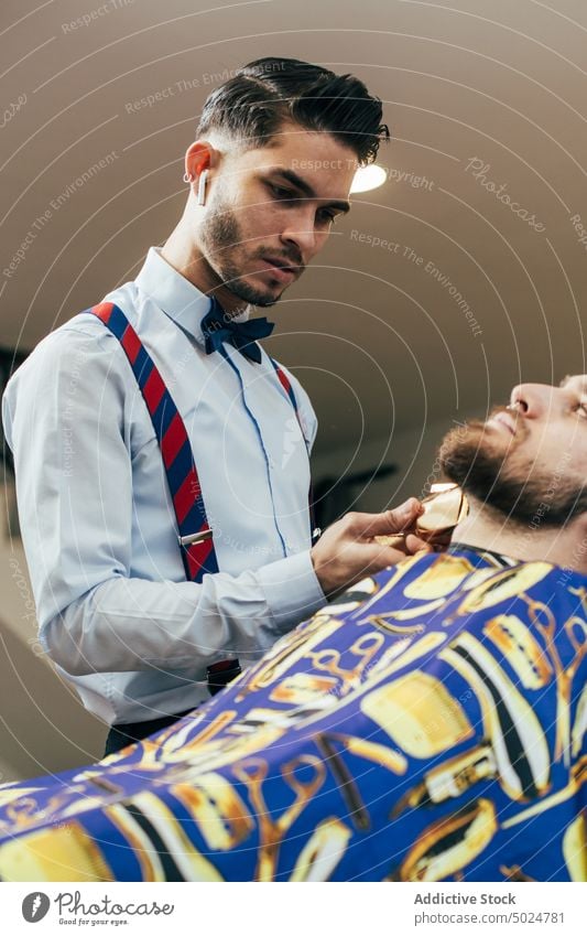 Barber working in a barbershop barber chair barber shop beard beauty care client clipper cut elegant haircut hairdresser hands head indoor lifestyle male man