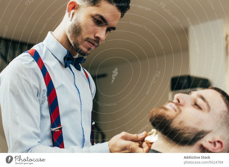 Barber working in a barbershop barber shop beard beauty care client clipper cut elegant hair haircut hairdresser hands head indoor lifestyle male man modern