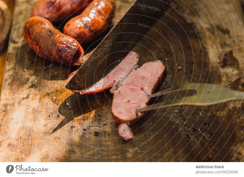 Knife above delicious grilled sausage on cutting board pork meat nutrition protein food knife carving fork utensil shade chopping board aroma half tasty
