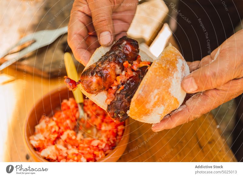 Crop man preparing sandwich with sausage and chopped vegetables prepare bread lunch savory tasty grilled bowl cut tomato onion wheat piece tender soft baked