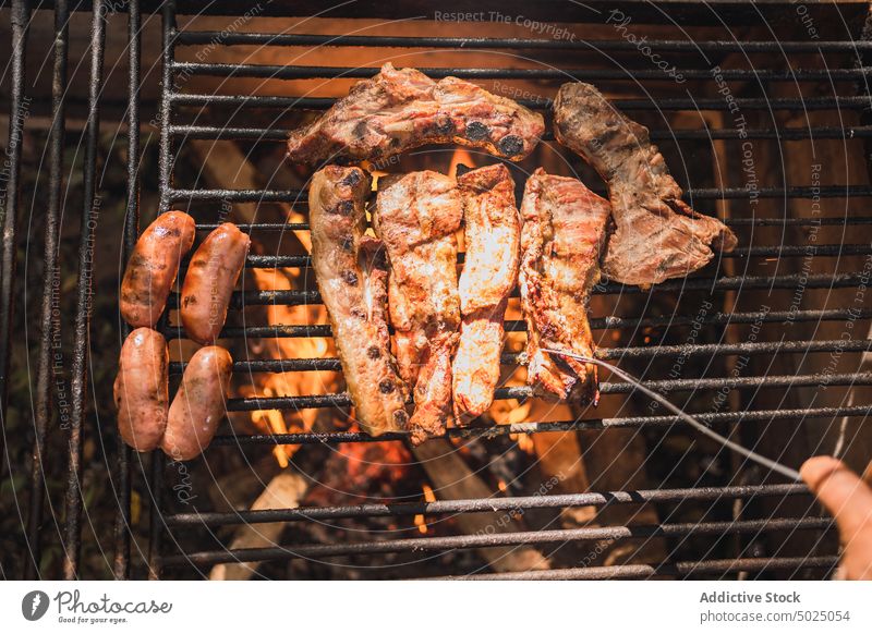 Crop person grilling delicious meat pieces above fire sausage barbecue food protein nutrition rack aroma pork tasty appetizing tender burn flame hot natural