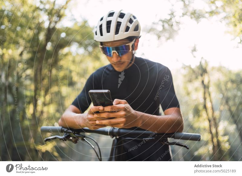 Cyclist on bike chatting on smartphone in forest bicyclist internet online sport cycle man woods using gadget creative design helmet cellphone style modern
