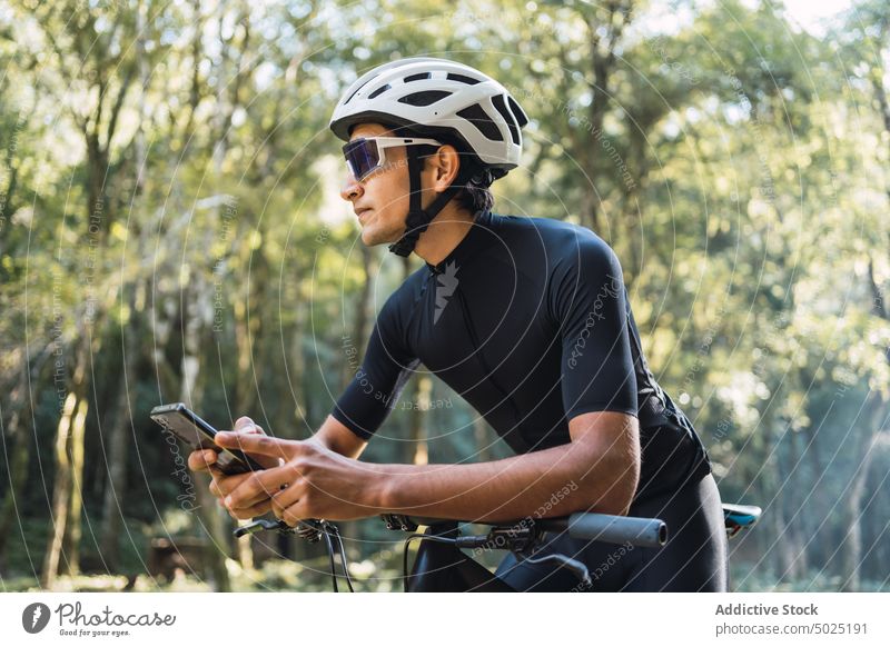 Cyclist on bike chatting on smartphone in forest bicyclist internet online sport cycle man woods using gadget creative design helmet cellphone style modern