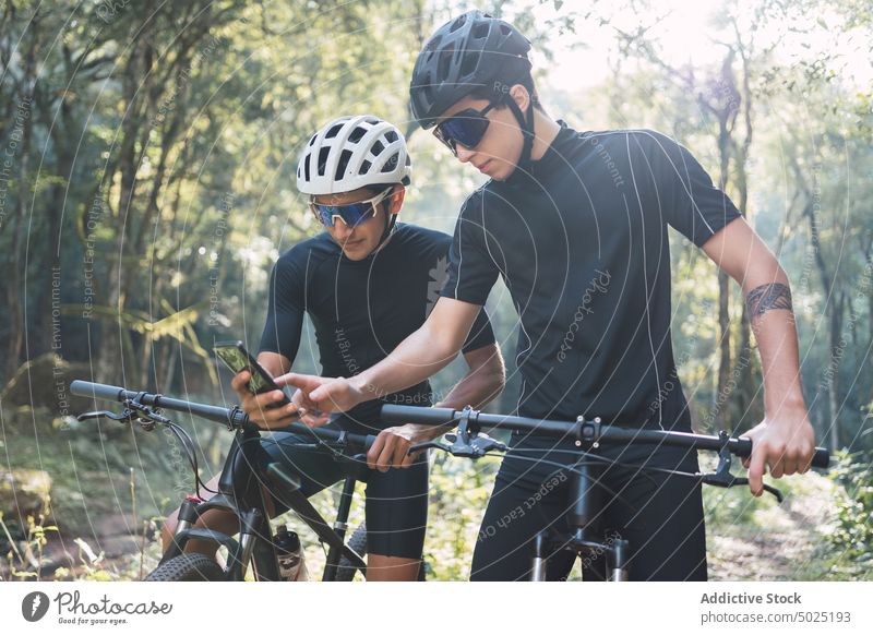Cyclists using GPS on smartphone having bike trip in woods men gps bicycle app orientate route navigate cyclist direction share sport gadget interact device