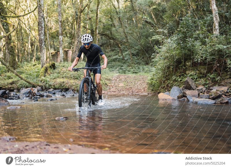 Cyclist riding bicycle in shallow river in forest cyclist ride bike sport trip activity man foam water splash active bicyclist woods nature splatter exercise