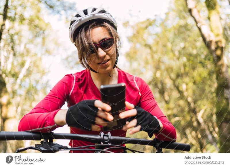 Bicyclist on bike browsing on smartphone in forest bicyclist surfing moment sport woman message text from below woods using gadget device training workout cycle