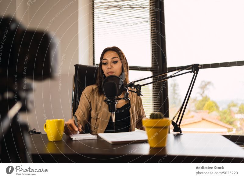 Woman on radio station writing on a notepad woman host headphones microphone take note notebook broadcast female blog pen write record workplace wireless