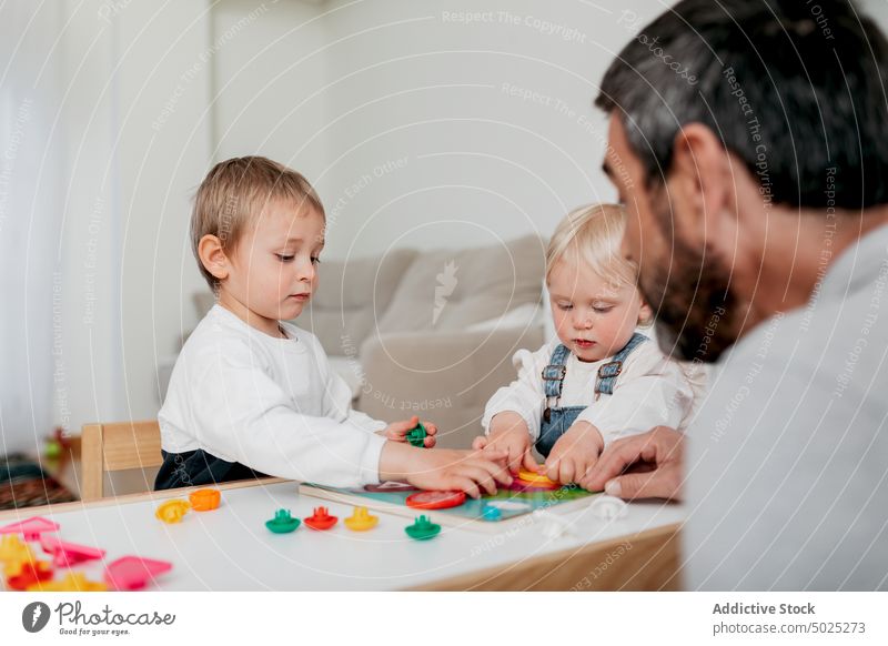 Crop dad interacting with charming children at home father board game play childcare education fatherhood childhood table man assemble sibling kid talk piece