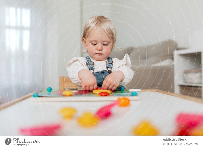 Cute girl playing board game at home assemble piece stare childhood charming portrait toddler innocent sweet table intent gaze denim sit friendly gentle stupor