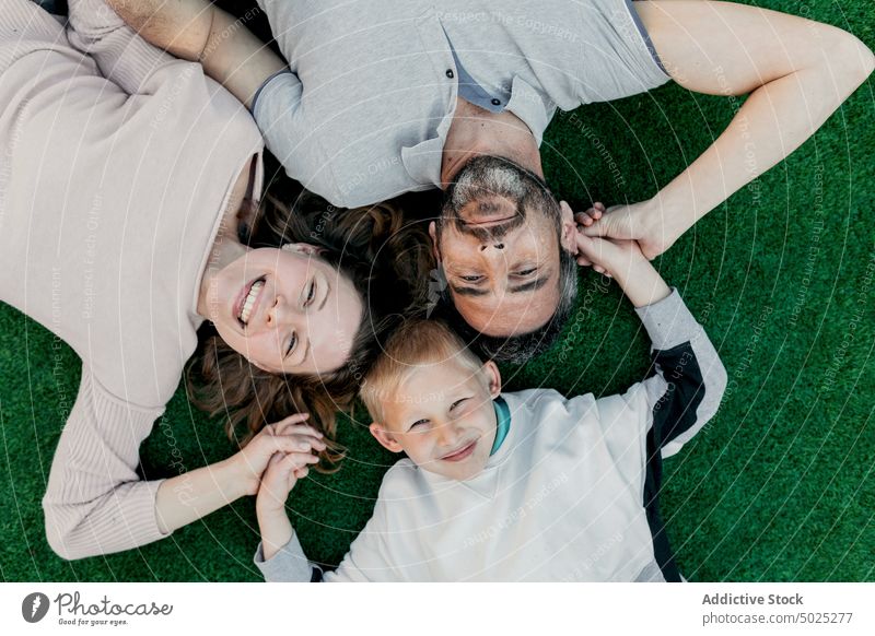 Happy family holding hands while resting on lawn son content love carefree candid portrait childhood parenthood smile idyllic harmony meadow lying grass happy