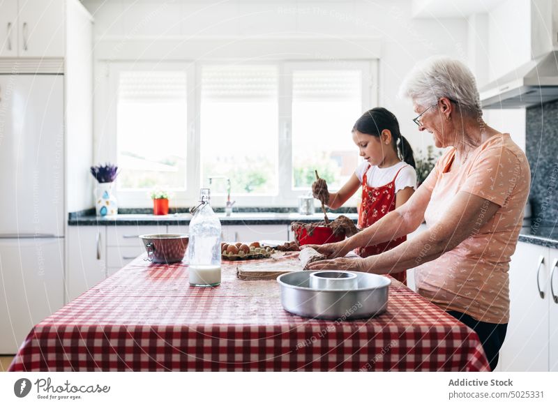 Smiling grandmother with girl preparing dough at home granddaughter cook culinary recipe cheerful spend time kitchen homemade woman rolling pin flour
