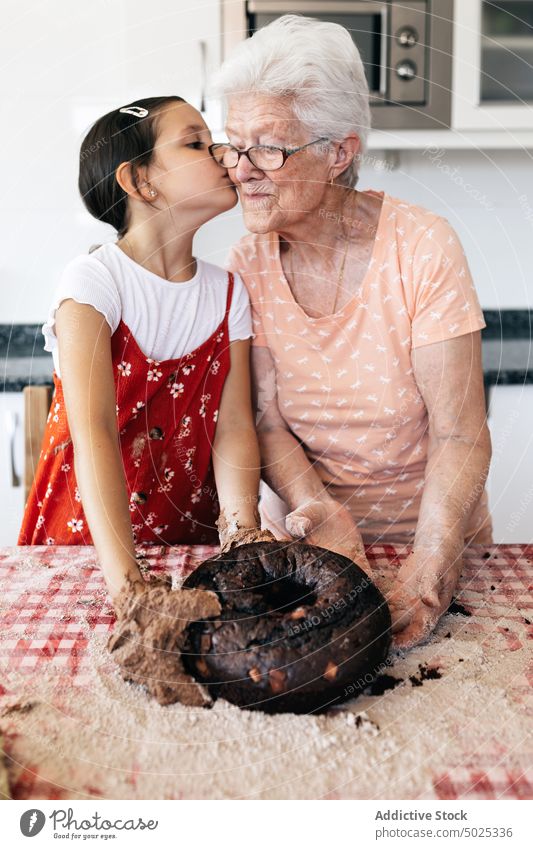 Granddaughter kissing grandmother while cooking in kitchen grandma granddaughter culinary recipe prepare dough help embrace woman love girl spend time bonding