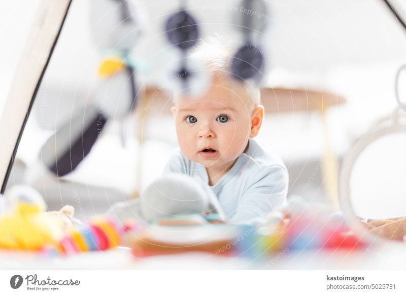 Cute baby boy playing with hanging toys arch on mat at home Baby activity and play center for early infant development. Baby playing at home newborn childhood