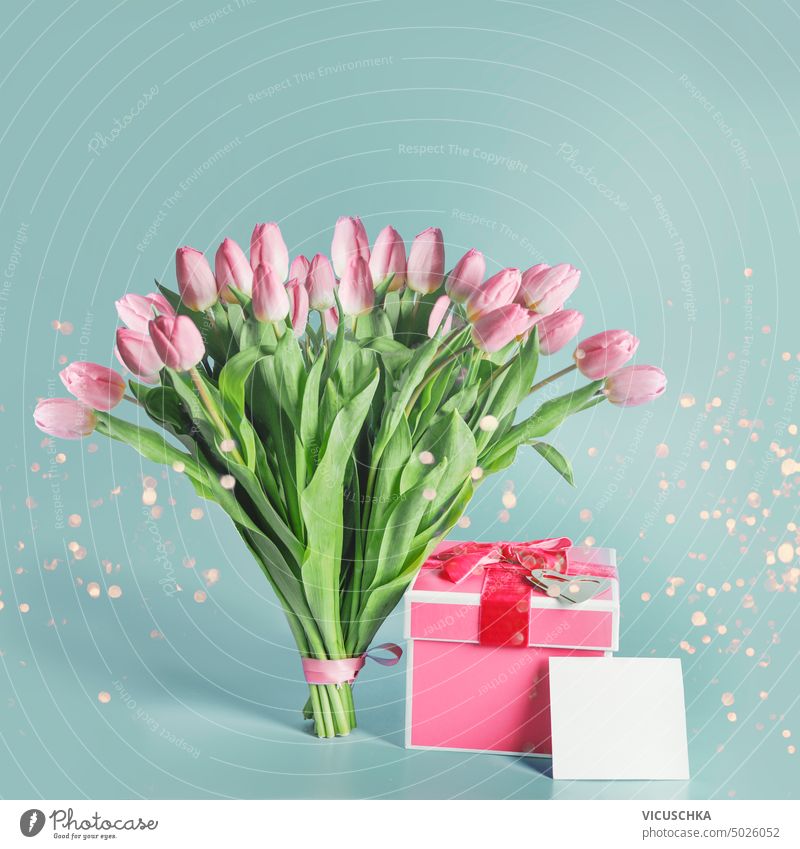 Beautiful pink tulips bunch with gift box, greeting card mock up and bokeh at blue background. beautiful bright green objects birthday holiday anniversary