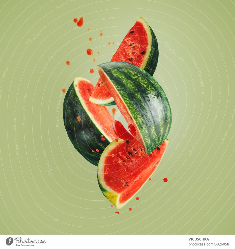 Flying watermelon quarters with juice splash drops at green background, front view. Food levitation flying food design sweet objects healthy minimal creative
