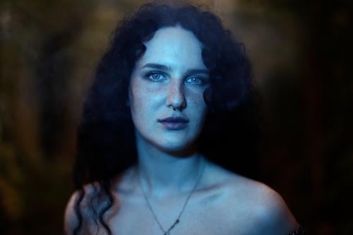 Close portrait of young dark haired woman with curls, light blue eyes and freckles in blue green light Woman Young woman Freckles Curl Brunette long hairs pale