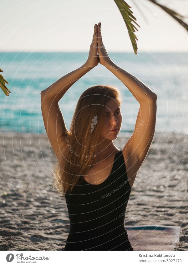 Beautiful young woman practicing morning yoga in lotus pose on tropical sea beach with tree palms. female fitness meditation balance exercise girl health