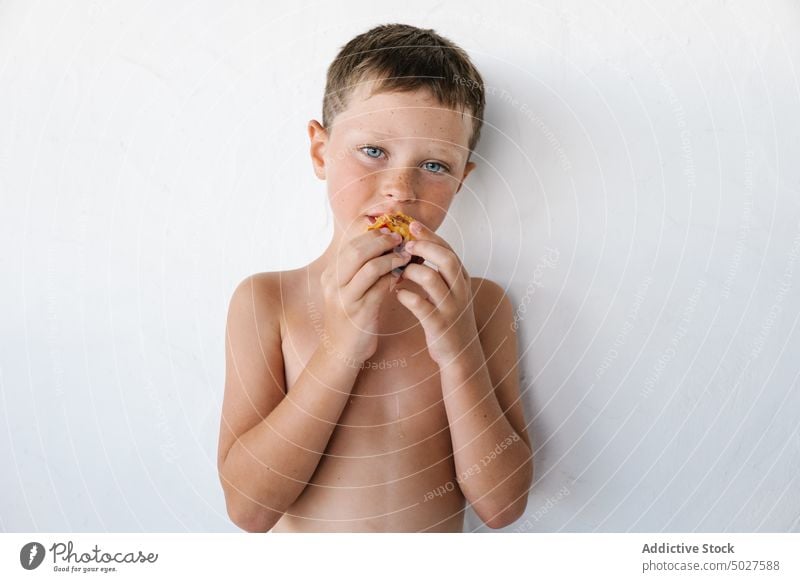 Adorable shirtless little kid eating yummy fruit against white wall child nectarine excited delicious healthy food boy funny portrait happy tasty positive sweet