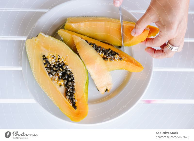 Crop anonymous person cutting papaya with knife fruit food vitamin exotic fresh tropical delicious ripe whole plate hand daylight healthy food summer season