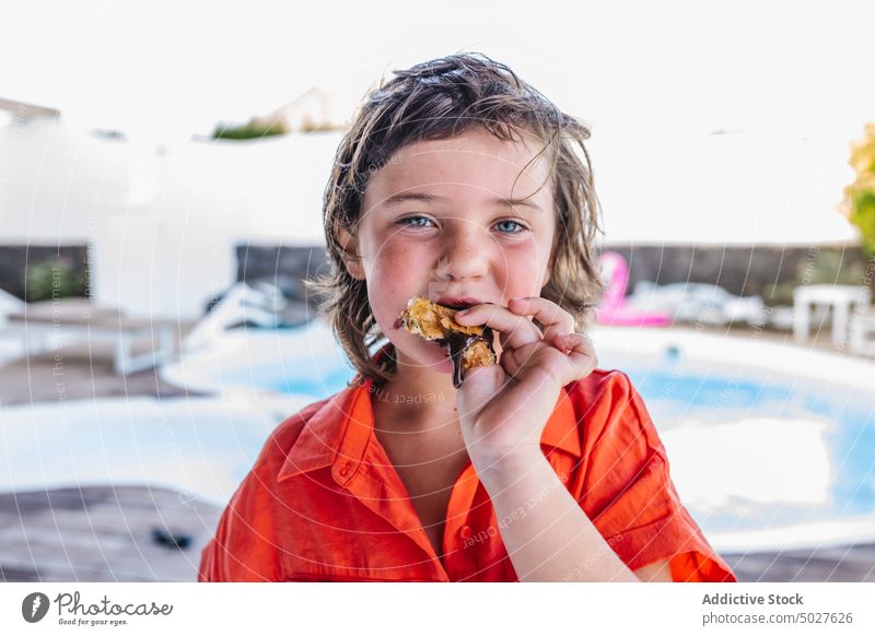 Adorable child eating chocolate crepe at poolside holiday dessert hungry boy portrait summer childhood positive sweet kid cute brown hair shirt resort content